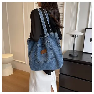 Detail of blue washed denim tote bag featuring brown leather logo patch and front pocket