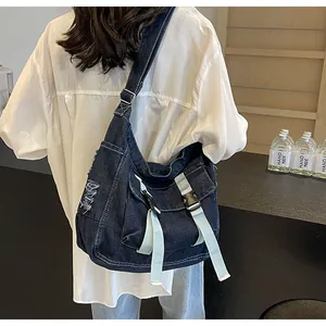 Detail of distressed denim crossbody bag with fringe accents and buckle straps on a model