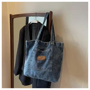 Detail of blue washed denim tote bag featuring large pocket and leather patch on blazer