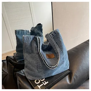 Detail of blue washed denim tote bag featuring a leather patch pocket and shoulder straps
