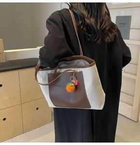 Detail view of canvas and leather tote bag featuring a cute orange knitted persimmon charm