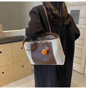 Detail of canvas tote bag with brown leather pocket and a knit persimmon charm accessory