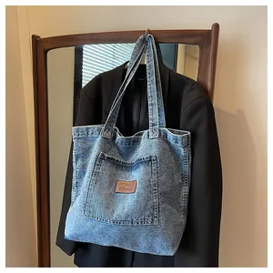 Close-up of vintage washed denim tote bag featuring a leather logo patch on large pocket