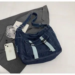 Detailed view of dark blue denim messenger bag with frayed edges and buckle pockets