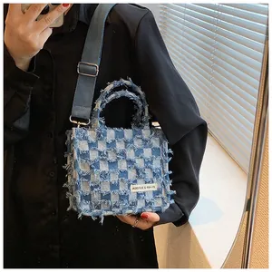 Detail of blue checkerboard denim tote with fringe edges and wide fabric shoulder strap