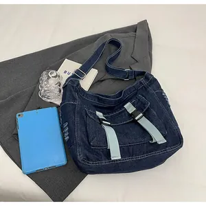 Detail of denim crossbody messenger bag with buckle closure and side distressed fringe