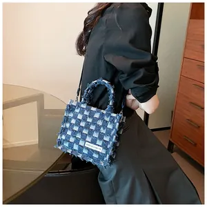 Detail of blue checkerboard denim tote bag with raw edges and detachable strap worn by model