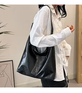 Détail du grand sac cabas noir brillant plissé porté par un mannequin au style minimaliste