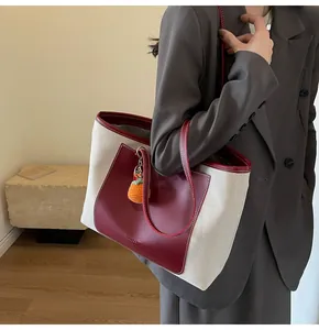 Detail of canvas and burgundy leather tote bag with orange woven charm on model