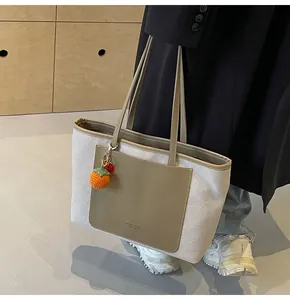 Detail of canvas tote bag with olive green leather pocket and orange charm