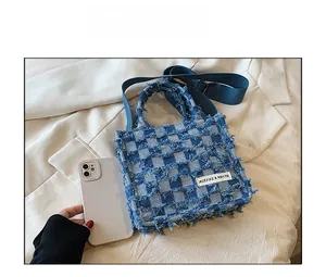 Detailed top view of a denim checkered tote bag with frayed edges and adjustable strap