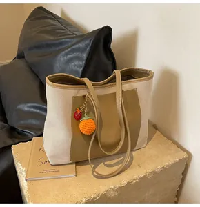 Detail view of canvas tote bag featuring brown leather pocket and persimmon charm