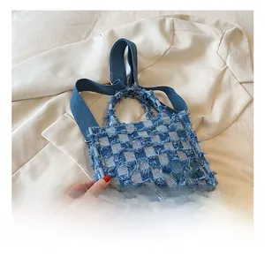 Detail of blue checkerboard denim tote bag with frayed edges and fabric brand label