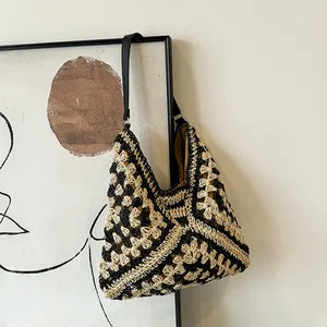 Detail of hand-woven straw tote bag with black and white geometric pattern and leather strap