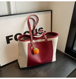 Detail of canvas tote bag with burgundy leather pocket and woven persimmon charm