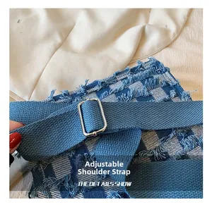 Detail of adjustable blue fabric shoulder strap with silver buckle on checkered denim tote