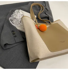 Detail of two-tone tote bag with woven texture, leather panel and orange crochet charm