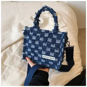 Detail of blue checkered denim tote bag with frayed edges and brand label on white suit
