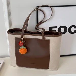 Minimalist beige canvas tote bag with brown leather trim and orange crochet charm