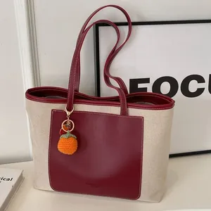 Minimalist canvas and burgundy leather tote bag with orange knit charm for daily commute