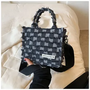 Detailed view of black and white checkered denim tote bag with frayed edges and logo patch