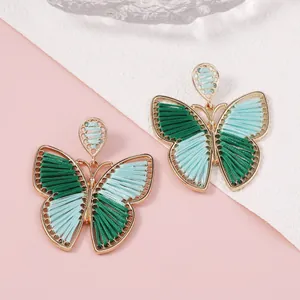 Detalle de pendientes de mariposa hechos a mano con hilos de seda verdes tejidos