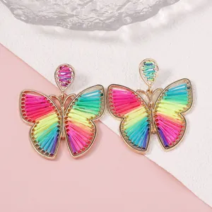 Pendientes de mariposa hechos a mano con marcos dorados e hilos tejidos de colores sobre fondo rosa