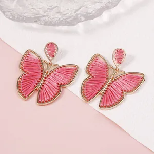 Detalle de pendientes de mariposa hechos a mano con bordado rosa y marcos dorados