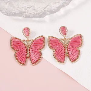 Primer plano de pendientes de mariposa tejidos en rosa con marco de aleación dorado fino