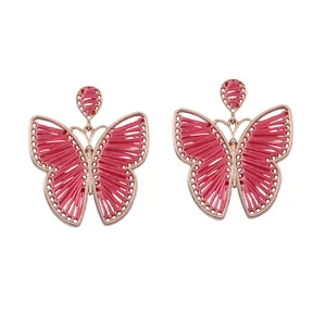 Detalle de aretes de mariposa hechos a mano con hilo rosa y marco de aleación de oro