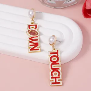 Detailed view of asymmetric gold-tone football earrings with TOUCHDOWN lettering and pearls