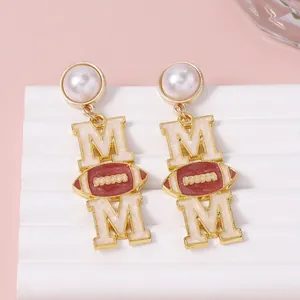 Boucles d'oreilles MOM dorées avec motif rugby et perles sur présentoir élégant