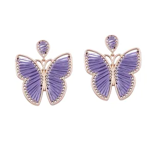 Detalle de pendientes de mariposa tejidos en color púrpura con marcos de oro rosa