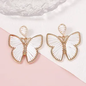 Detalle de pendientes de mariposa hechos a mano con marco de aleación dorada y hilo blanco