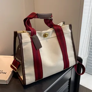 Beige canvas draagtas met rode strepen en bruine lederen rand op een zwart kastje