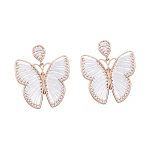 Detalle de pendientes de mariposa hechos a mano con marco dorado y tejido de hilo blanco