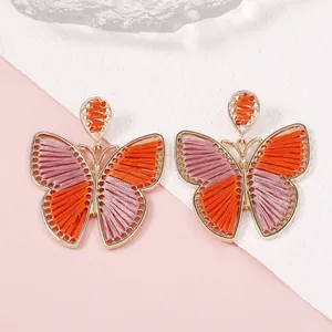 Detalle de pendientes de mariposa tejidos a mano con hilos de seda naranja y rosa