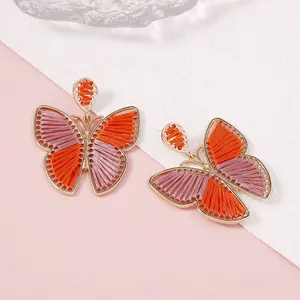 Detalle de pendientes de mariposa hechos a mano con hilos de bordado naranja y rosa
