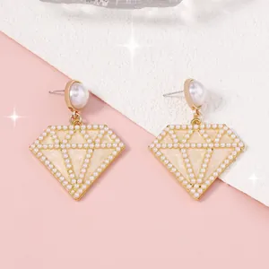 Detalle de pendientes geométricos dorados con perlas y esmalte blanco elegante