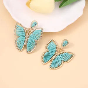 Primer plano detallado de pendientes de mariposa tejidos a mano con marco dorado y seda verde