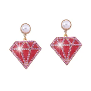 Detalle de pendientes con perla blanca y colgante de rombo rojo con brillantes pedrería rosa