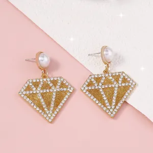 Detalle macro de pendientes colgantes geométricos dorados con perlas y circonitas