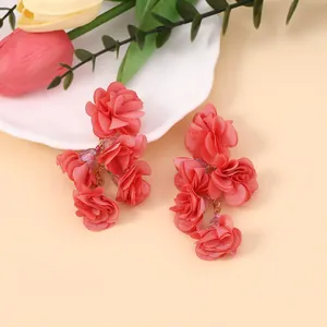 Detail von roten Chiffonblumen-Ohrringen auf einem dekorativen weißen Tablett