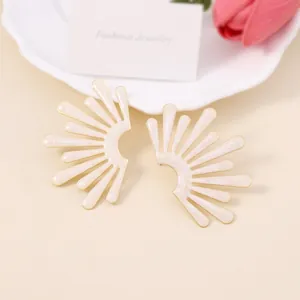 Eleganti orecchini a forma di ala dorati con smalto crema su un vassoio di ceramica