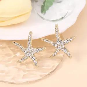 Macro shot of gold starfish earrings with cubic zirconia on textured glass surface