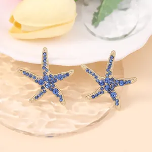 Close-up of starfish earrings with blue zircons on wavy glass for beach style