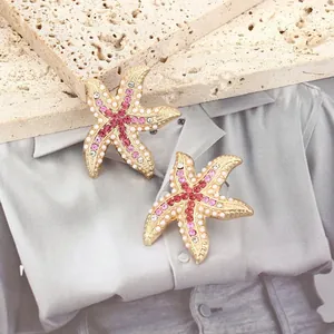 Dettaglio macro di orecchini a stella marina con strass rosa e perle bianche