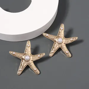 Detail of golden starfish earrings with center pearl and beaded tips on gray background