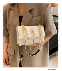 Detail of white quilted crossbody bag featuring a gold S logo with tassel and chain strap