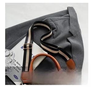 Detail of wide fabric shoulder strap and gold hardware on brown quilted handbag